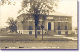 A sepia-toned photo of a large brick building with arched windows and columns at the entrance. A tree stands in front, and a few houses are visible in the background. A sign reads Library, Southbridge, Mass.