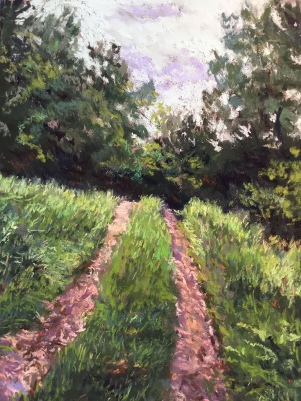 A dirt path with grass growing in the center runs through tall green grass and trees under a cloudy sky, suggesting a peaceful, natural landscape in late spring or summer.