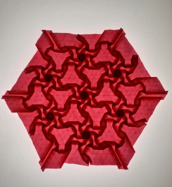 A hexagonal piece of red paper folded into an intricate, geometric origami tessellation with repeating star-like and spiral patterns.